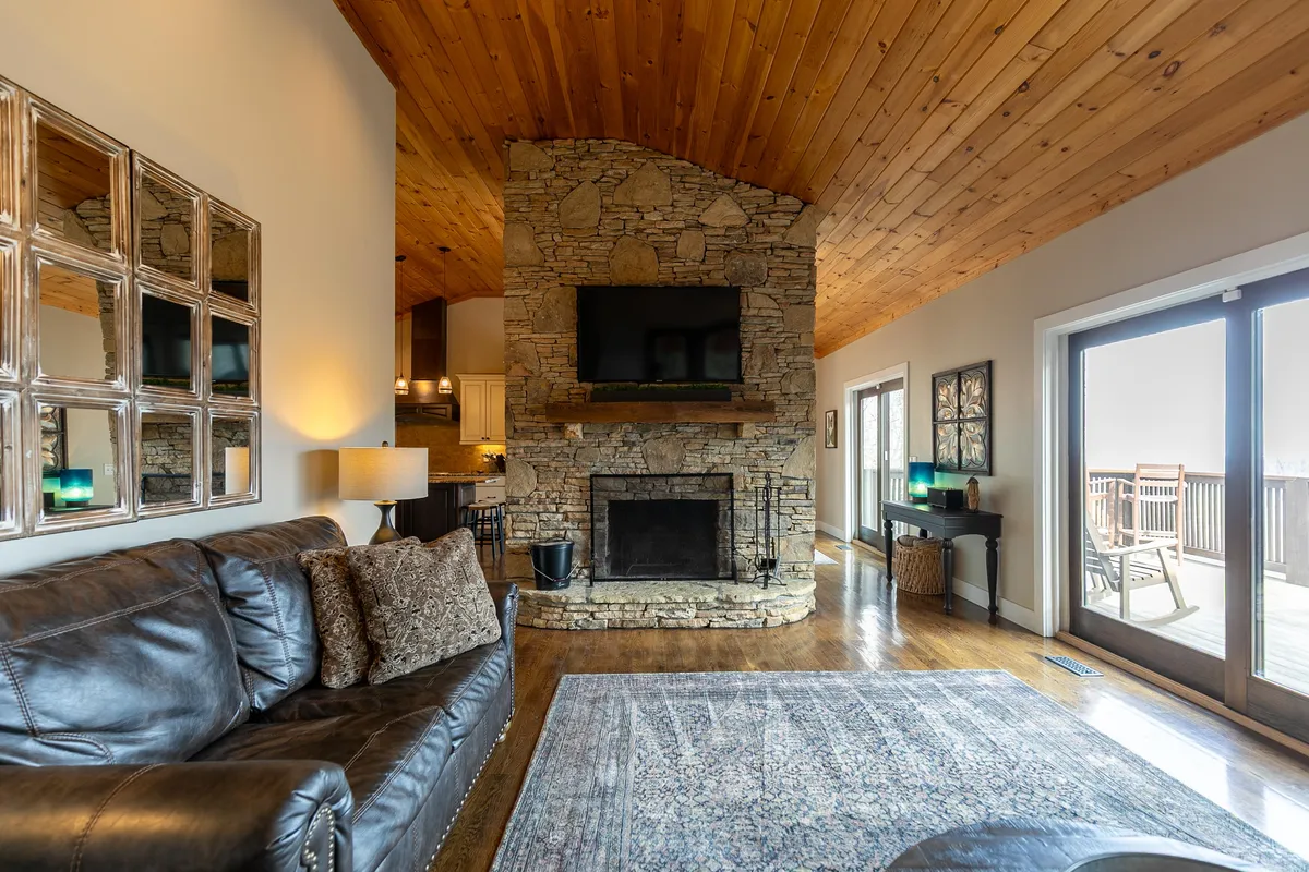 A spacious living area featuring a stone fireplace, a comfortable leather sofa, and large windows that offer views of the outdoors. The room is designed for entertaining and relaxing, making it ideal for group gatherings. The natural light and connection to the exterior scenery enhance the atmosphere.