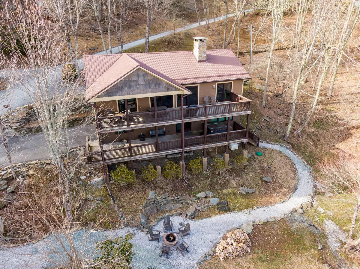 A view of the house exterior featuring an upper balcony and a landscaped path leading to a fire pit area. The fire pit is surrounded by chairs, inviting guests to gather for s’mores and stargazing, with the serene mountain landscape as a backdrop.