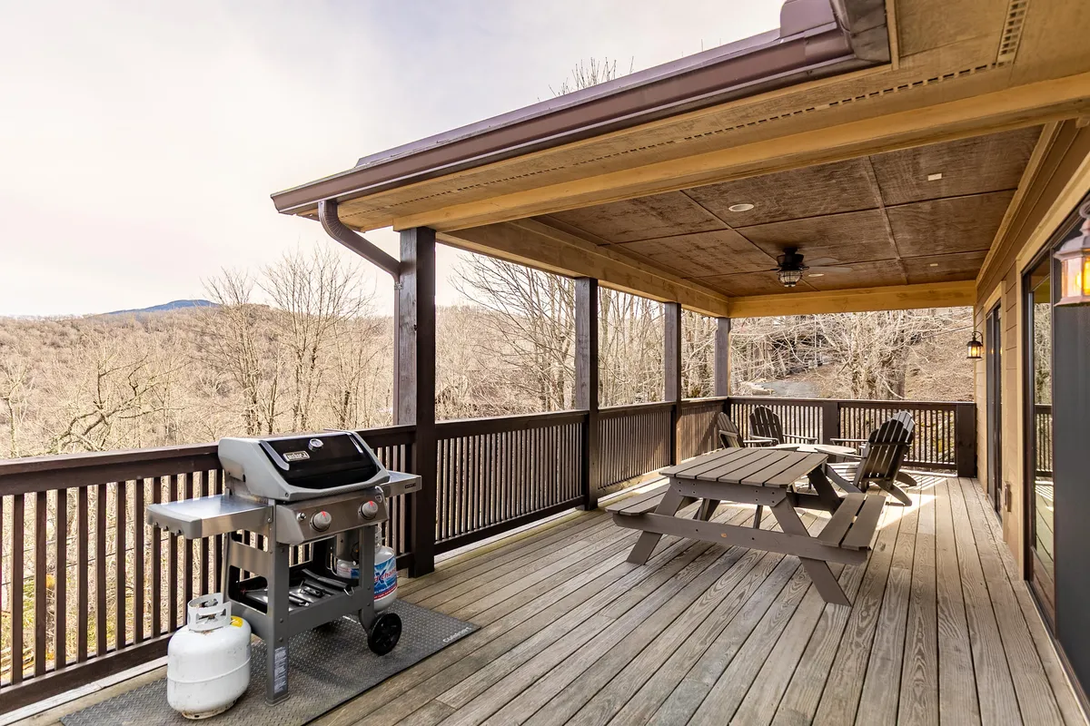 A lively exterior scene with a grill, picnic table, and rocking chairs set up under the open sky. The space is ideal for group barbecues, casual meals, and relaxing together while enjoying mountain views.