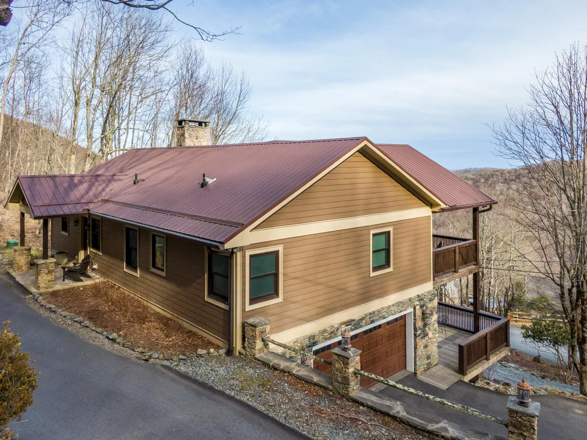 The image showcases the inviting exterior of a mountain cabin with a sturdy stone foundation and a classic metal roof. The spacious balcony overlooks sweeping mountain vistas, bathed in the soft glow of sunset. The setting exudes tranquility and invites guests to relax outdoors, surrounded by the serene beauty of nature.