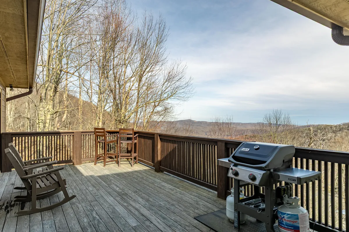This exterior image shows a deck outfitted with a grill, bar stools, and a sweeping view of the mountains. The setup is ideal for outdoor dining, gathering, and soaking in sunset or sunrise vistas.