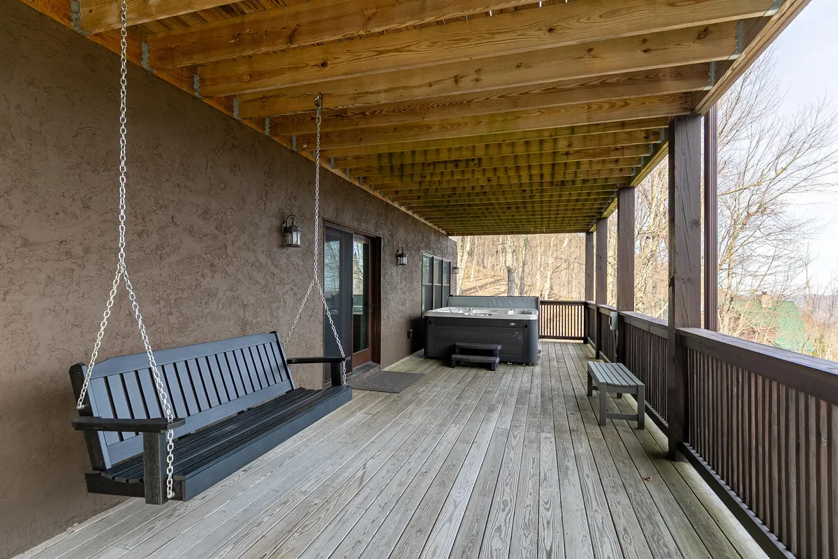 A cozy section of the wooden deck with a swing bench and hot tub, framed by sturdy beams and surrounded by lush nature. The scene feels private and welcoming, underlining opportunities for quiet moments and celebrating special occasions.