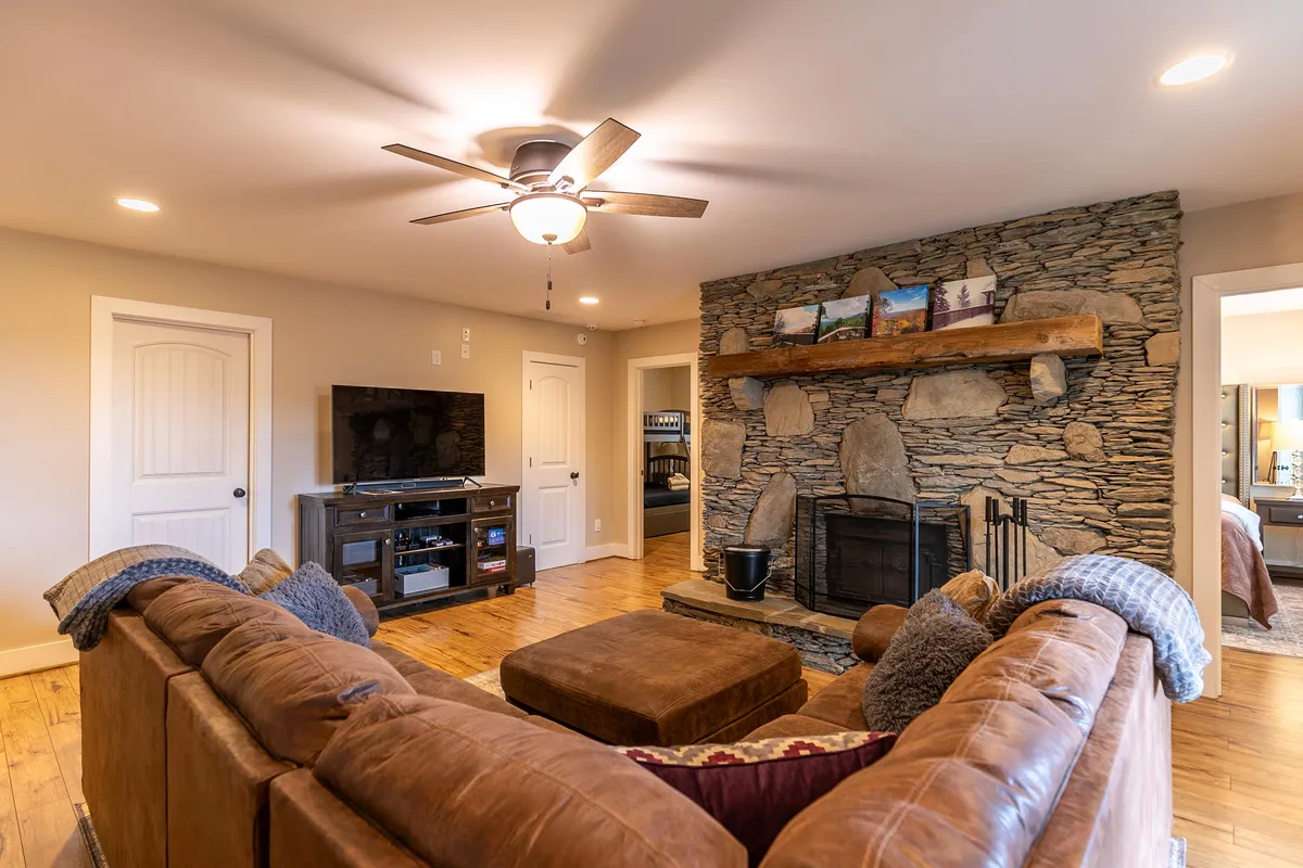 The living area is centered around a striking stone fireplace, with a comfortable sofa and warm wooden flooring. The space feels inviting and perfectly blends rustic mountain charm with stylish furnishings, ideal for cozy gatherings or quiet moments.
