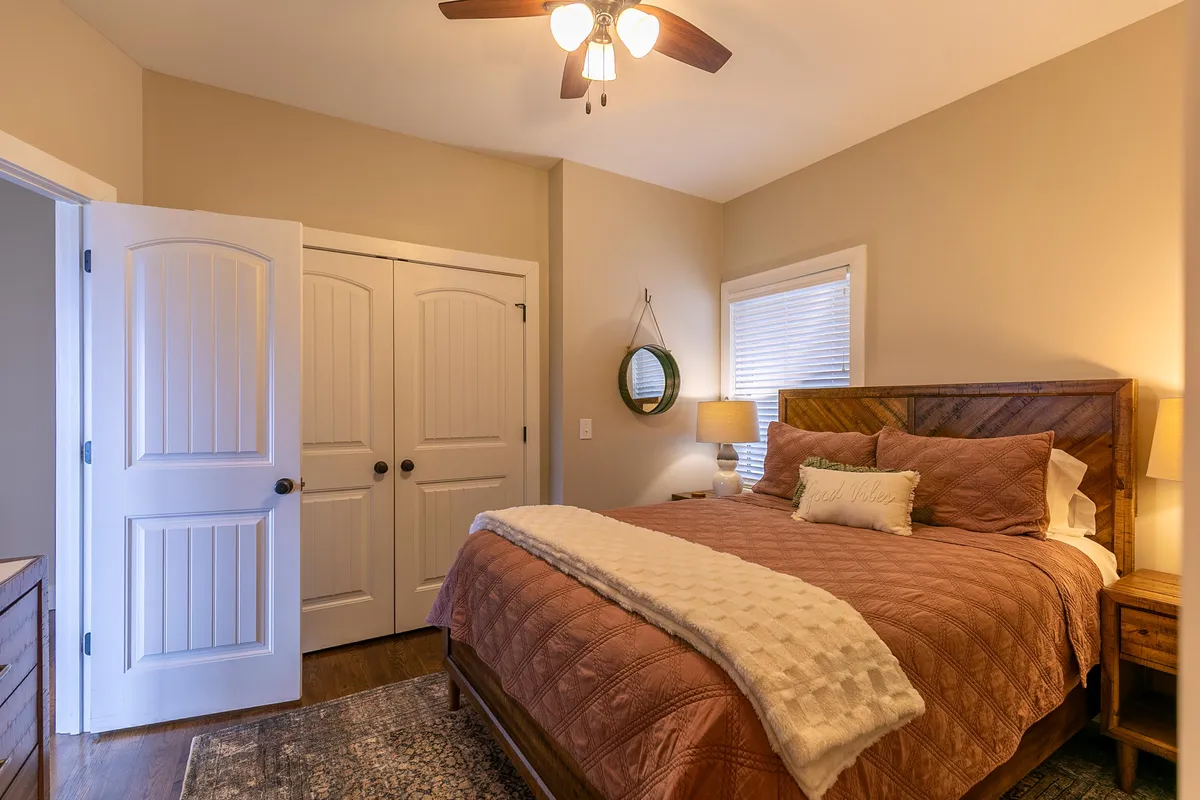 A restful guest bedroom with a cozy bed topped with decorative pillows, a nightstand with a warm lamp, and a wall mirror. The soft color palette and gentle lighting create a welcoming and tranquil environment for relaxation.
