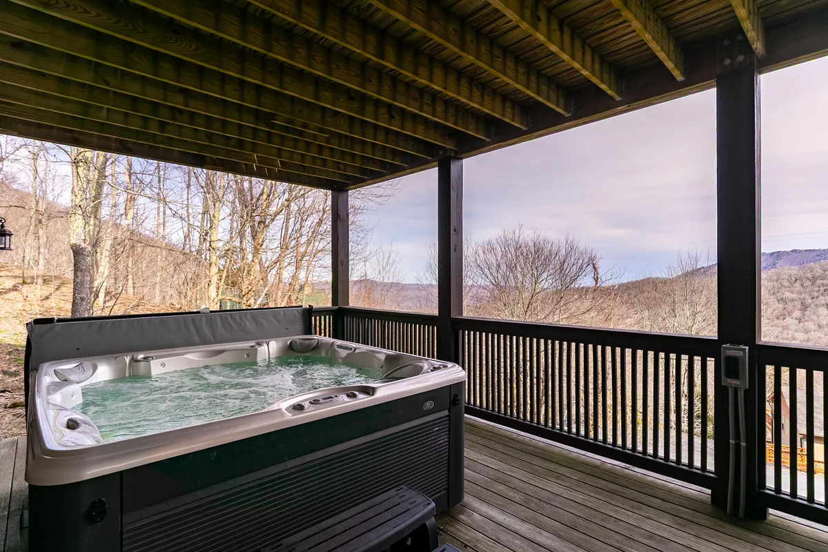 An exterior view featuring the hot tub overlooking rolling hills, with a wooden railing framing the mountain landscape. The serene setting invites relaxation and offers opportunities for stargazing or taking in the scenery after outdoor activities.