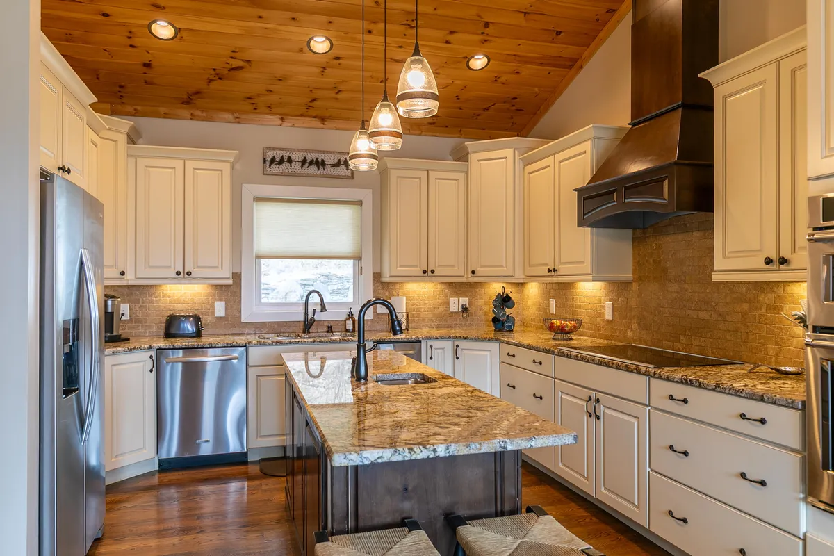A modern gourmet kitchen with granite countertops, stainless steel appliances, a central island with a secondary sink, and wooden ceilings. The space is organized for both cooking and entertaining, with inviting touches that make it a gathering spot.