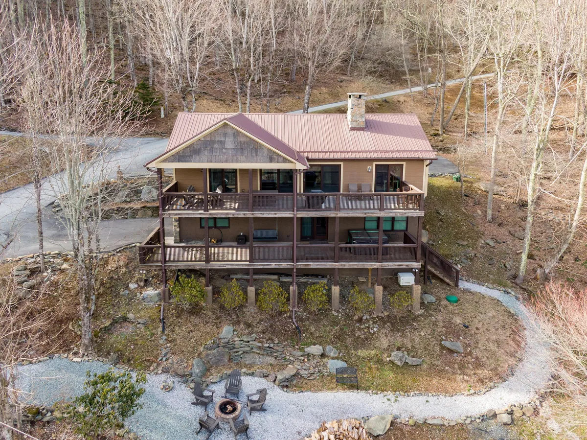 This exterior shot captures Starlight Ridge with its inviting porch, fire pit area, and the winding path through the surrounding woods. The home sits nestled among trees, suggesting immediate access to nature trails and outdoor adventure opportunities.