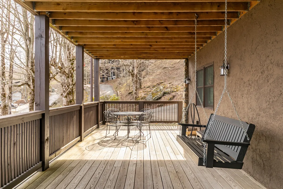 A tranquil porch area featuring a swinging bench and a small dining table beneath wooden beams. The setting is inviting for relaxed family moments, reading, or enjoying a sunrise together.