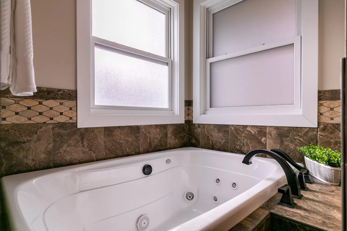 A tranquil bathroom centered on a jacuzzi tub set beneath a window streaming in natural light. The space is adorned with a decorative plant, creating a peaceful, spa-inspired ambiance ideal for relaxation and self-care.