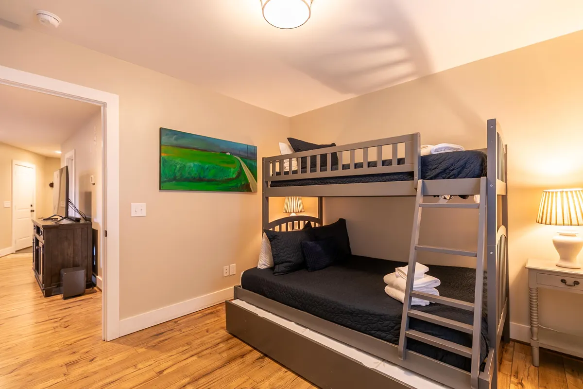 A cheerful kids’ bunk room featuring a sturdy bunk bed, playful wall art, and a handy nightstand with a lamp. The design is practical yet fun, inviting children to make memories and enjoy cozy nights together.